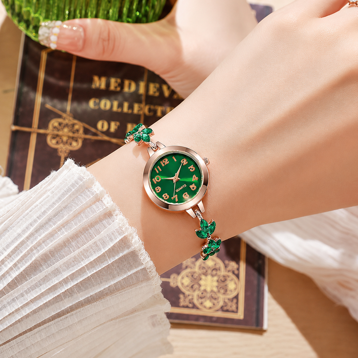 Luxury women's emerald green bracelet watch with rose gold adjustable slider chain and crystal leaf accents on a white stone background.