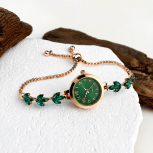 Luxury women's emerald green bracelet watch with rose gold adjustable slider chain and crystal leaf accents on a white stone background.